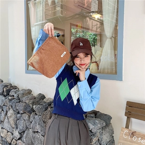 Brown corduroy clutch bag paired with a blue shirt and knitted vest in a cafe setting