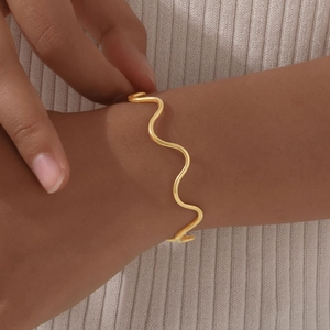 Detail shot of a wavy golden stainless steel bracelet worn on a female wrist