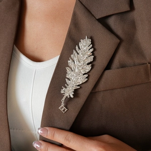 Silver feather brooch with rhinestones on brown blazer lapel close-up detail view