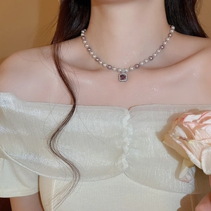 Close-up of pearl necklace with purple gemstone pendant on a model's neck
