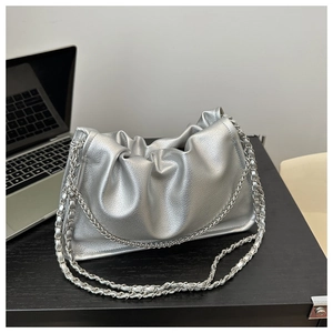 Close-up of metallic silver pleated dumpling bag with silver chain strap on table
