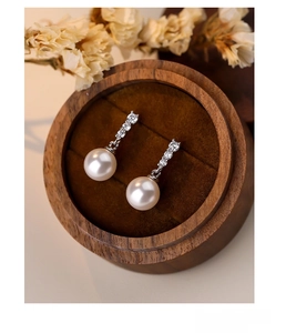 Macro shot of S925 silver pearl drop earrings on a wood jewelry box with dried flowers