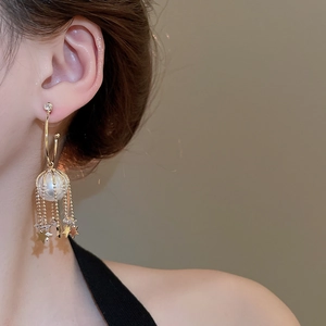 Detail view of golden tassel earring with star charm and pearl on model's ear