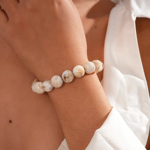 Detail of beaded bracelet with marble texture beads on wrist against white shirt