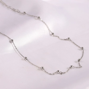 Close-up of silver stainless steel bead chain necklace on white silk background