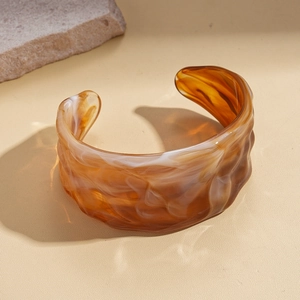 Detail of amber marble acrylic cuff bracelet with wavy pleated texture and open design