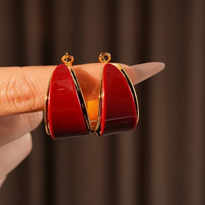 Detail of red resin C-shaped hoop earrings with gold trim worn by a model on a brown background