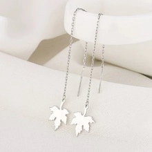 Détail de boucles d'oreilles pendantes en feuille d'érable argent sur fond minimaliste