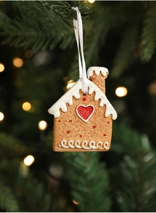 Macro detail of resin gingerbread house ornament hanging on a green Christmas tree