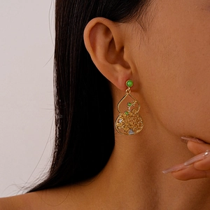 Detailed view of hollow gold filigree gourd earrings with green beads on model