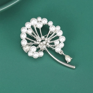 Détail de la broche pissenlit argentée avec perles et strass sur fond vert foncé