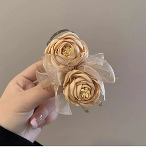 Detailed view of beige rose fabric flowers and translucent ribbon bow on a clear hair claw