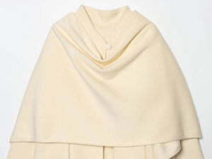 Detail of cream wool blend cape coat showing soft fabric texture and white button