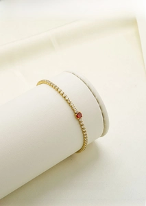 Detailed close-up of a gold tennis bracelet with white zircons and a red gemstone on a display