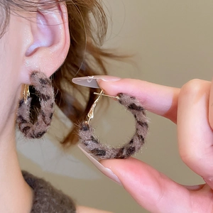 Detail view of leopard print plush hoop earrings with golden hooks on warm beige background