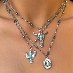 Close-up of layered silver necklace with cow skull, cactus, and turquoise pendant charms