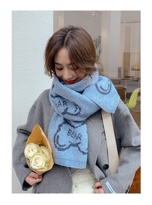 Detail of light blue knit scarf featuring cute bear patterns and EAR BEAR embroidery text