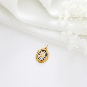 Détail macro du pendentif ovale doré avec lettre M et bordure rayonnante de soleil