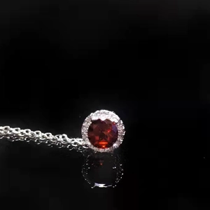 Detailed close-up of a round red gemstone pendant necklace with white diamond accents