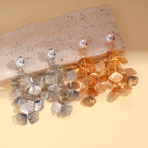 Metallic hollow ginkgo leaf earrings with pearls on textured stone surface