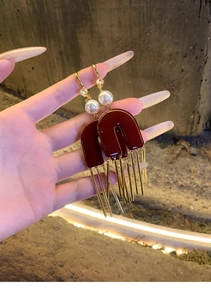 Detail of C-shaped burgundy acrylic earrings with white pearl and metal tassel pendants