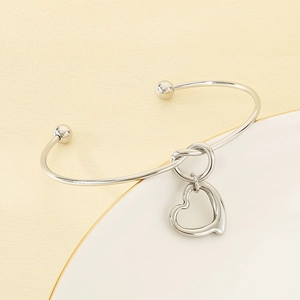 Close-up of silver hollow heart pendant on twisted stainless steel cuff bracelet