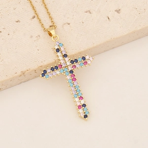 Close-up of 18K gold plated cross necklace with colorful zircons on a stone slab