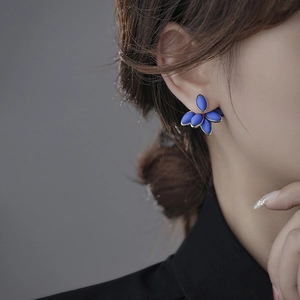 Close-up of elegant blue floral stud earrings featuring metallic edges on a model
