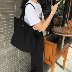 Detalle de un bolso de lona negro grande con texto blanco y correa de hombro ancha