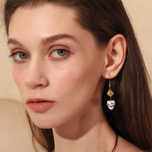 Macro detail of model wearing gold shell and blue-white porcelain heart earrings