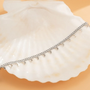 Detail of silver crescent moon pendants on a thin chain over a white shell background