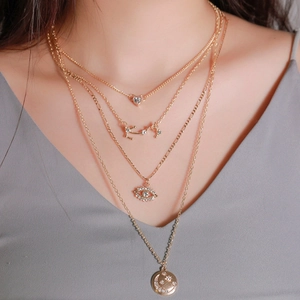 Detalle de collares en capas dorados con colgantes de corazón, ojo y luna