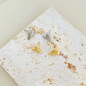 Macro view of minimalist 3D heart stud earrings in gold and silver on a textured stone base