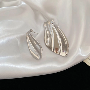 Macro shot of silver asymmetric liquid metal fishtail earrings on white satin fabric