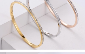 Detailed view of gold, silver, and rose gold bangles with zircon settings on a white stand
