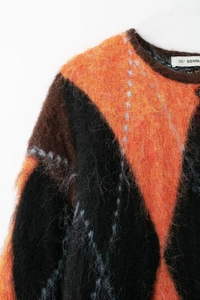 Gros plan d'un pull en maille à losanges moelleux avec des motifs orange et marron