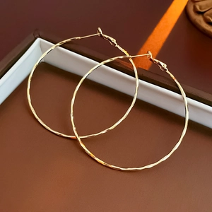 Detailed close-up of golden round hoop earrings with unique hammered metal texture in a gift box