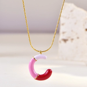 Close-up of golden letter C pendant with pink and red enamel on a delicate chain