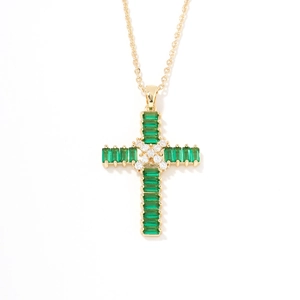 Close-up of gold cross pendant with emerald green gemstones and star-shaped crystal center