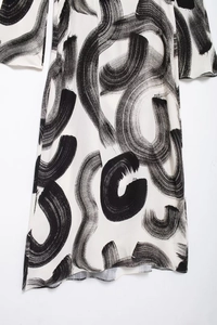 Detail view of white loose dress featuring black brush stroke patterns on high-quality fabric