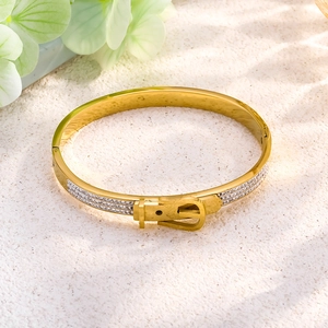 Gold belt buckle bangle with triple row of zircons on a textured white background