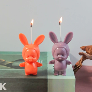 Handmade 3D rabbit ear baby scented candles in orange and purple on a book decor