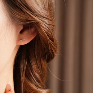 Close-up of gold-plated bar stud earrings with small clear cubic zirconia on the ear