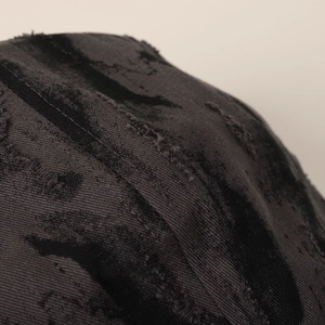 Detail of distressed dark grey cotton twill fabric with ripped texture and tie-dye patterns