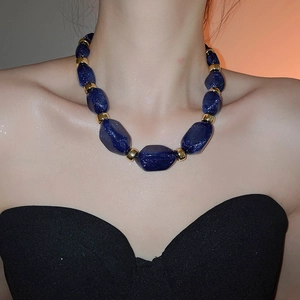 Close-up of deep blue irregular acrylic beads necklace with golden metal spacers on neck