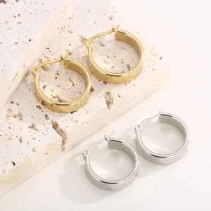 Detail of wide stainless steel hoop earrings in gold and silver finishes on stone.