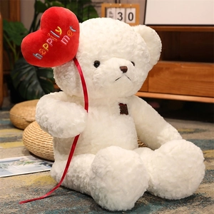 Close-up of a white teddy bear holding a red plush heart with embroidered text happily met