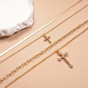 Close-up of layered gold cross necklaces with snake chain and rhinestone cross pendant