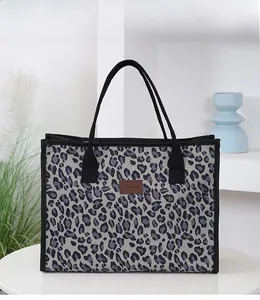Detailed view of leopard print tote bag with brown leather logo patch on white table