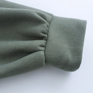 Close-up of gray-green wool coat sleeve showing refined fabric texture and pleated detail